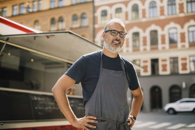 Portrait of confident chef standing by food truck on street in city