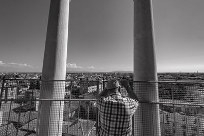 Rear view of man looking at buildings in city from balcony