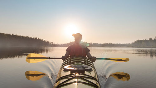 Rear view of man in lake against sky during sunset