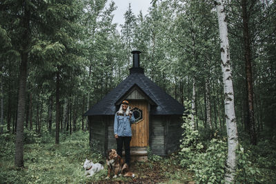 Woman standing in front of wooden hut in forest