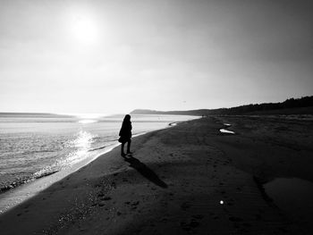 Silhouette woman walking at beach against sky