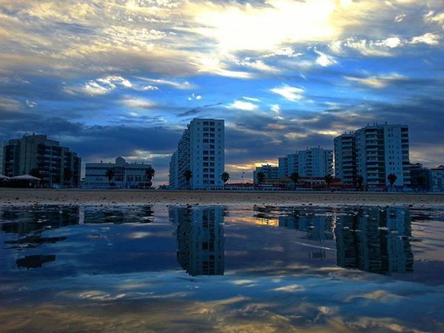 building exterior, architecture, built structure, city, water, sky, reflection, cloud - sky, skyscraper, waterfront, modern, cityscape, office building, cloud, building, river, urban skyline, tall - high, sunset, cloudy