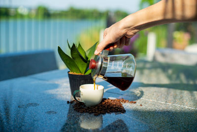 Hand of barista pouring the coffee from the glass jar into the cup at the outdoor garden