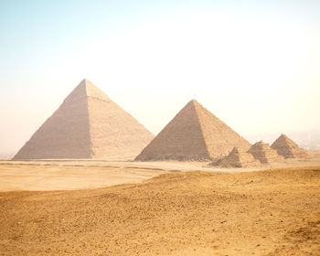 Scenic view of desert and pyramids of giza against clear hazy sky in the morning