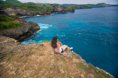 High angle view of woman sitting on cliff by sea