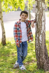 Portrait of boy standing by tree at park