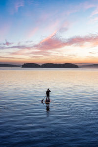 Silhouette man standing in sea against sky during sunset