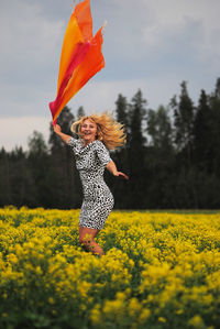 Happy young woman jumping with scarf amidst yellow field