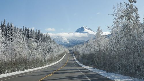 Empty road amidst snow covered mountains against sky