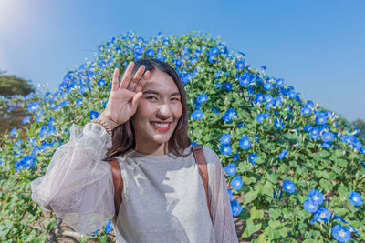 Portrait of smiling young woman standing against blue sky