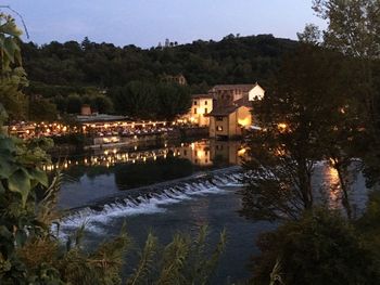 Illuminated buildings by lake against sky at night