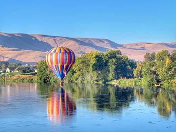 Hot air balloon touching down on river, reflection, trees and mountains in background, prosser, wa