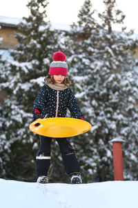 Winter portrait of children with a plastic sled sliding on a snowy slope and making a snowman