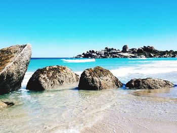 Panoramic shot of rocks on beach against clear blue sky