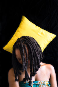 Woman and yellow cushion against black background