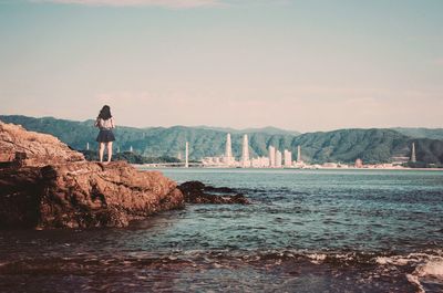 Rear view of woman standing on rock by sea against sky