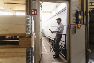 Mature man using digital tablet while standing by delivery truck at factory