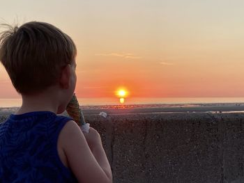 Rear view of boy on beach against sky during sunset