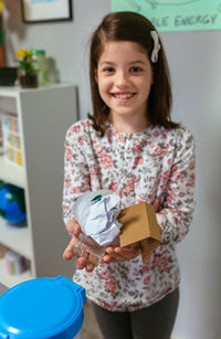 Smiling girl in an ecology classroom showing a handful of waste to recycle