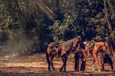 Men wearing hat standing with horse at forest