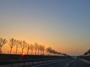 Road by silhouette trees against clear sky during sunset