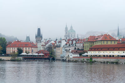Buildings of lesser town and devil stream called certovka by vltava river against cloudy sky, prague