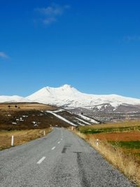 Road leading towards snowcapped mountain against blue sky