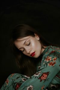 Close-up of beautiful young woman with eyes closed sitting against black background