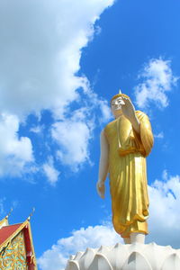 Low angle view of gold buddha statue against sky