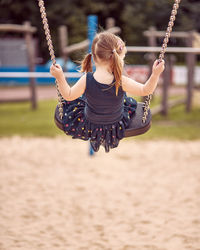 Rear view of girl playing on swing in playground