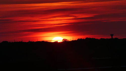 Silhouette trees on landscape against orange sky