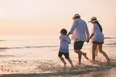 Family holding hands while walking in sea at sunset
