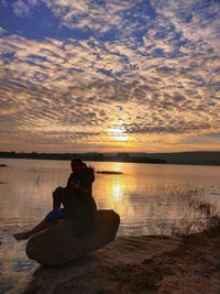 Woman sitting on beach against sky during sunset