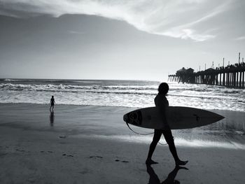 Silhouette woman with surfboard at branch against sky