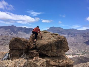 Rear view of man climbing on mountain against sky
