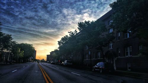 Road passing through city against cloudy sky