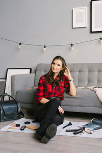 Young female makeup artist is sitting on the sofa floor next to randomly scattered brushes, makeup