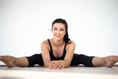 Portrait of smiling young woman sitting on table against white background