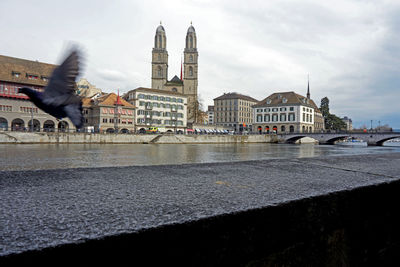 View of city at waterfront against cloudy sky