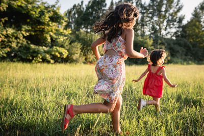 Two girls in dresses running one after another in the evening in the field