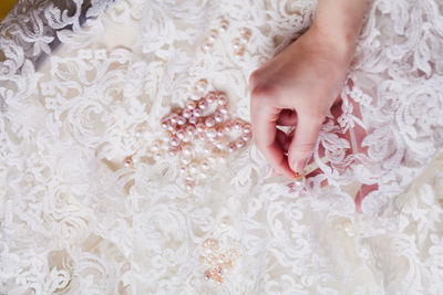 Cropped hand of woman stitching pearls on white wedding dress