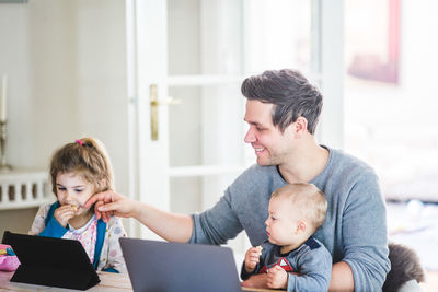 Smiling father sitting with son while touching girl watching movie on digital tablet at home