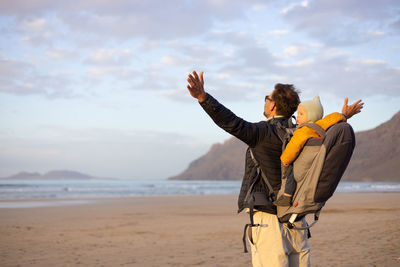 Rear view of woman standing at beach against sky