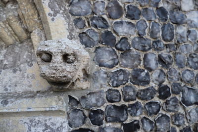 Close-up of a gargoyle against flint stone wall.