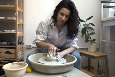 A potter in white shirt and blue jeans makes a bowl or vase on a fast spinning potter's wheel.