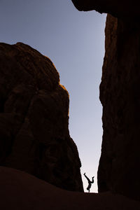 Low angle view of silhouette man practicing handstand amidst rock formations