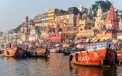 Boats moored in ganges river by old buildings against sky