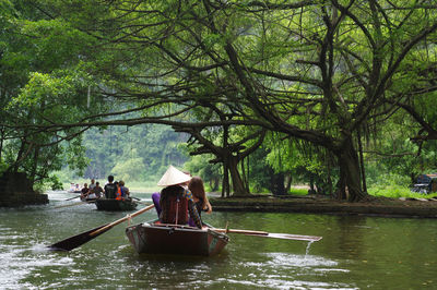 People sitting on rowboats in river at forest