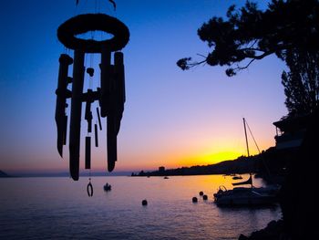 Silhouette wind chime hanging by lake against sky during sunset