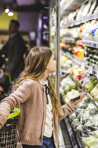 Side view of girl looking at vegetables on shelves in store